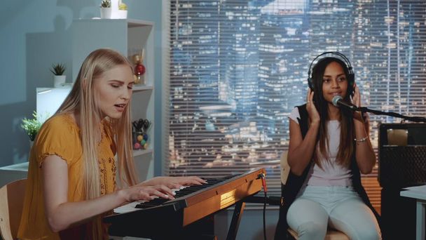 Красивые девушки поют песню, в то время как одна из них играет на клавиатуре во время репетиции дома
 - Фото, изображение