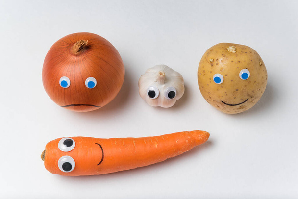 Gemüse mit Googleaugen auf weißem Hintergrund. Zwiebeln, Knoblauch, Kartoffeln, Karotten mit lustigen Gesichtern. - Foto, Bild