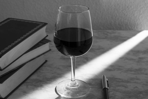 Copa de vino acompanada de unos libros y una camara fotografica con la luz de la venta entrando por un costado en blanco y negro - Φωτογραφία, εικόνα