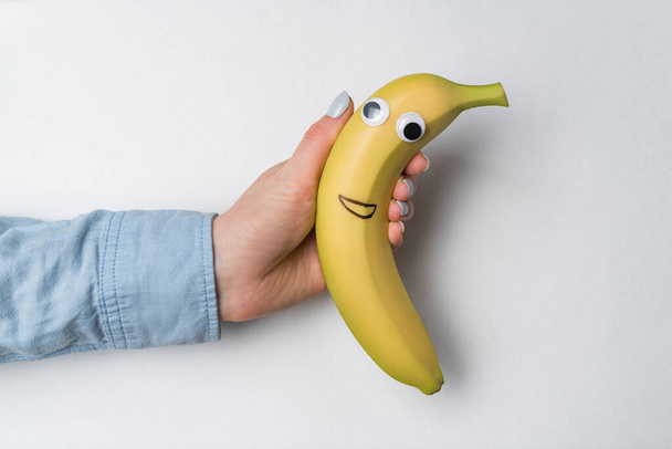 Ręka gospodarstwa zabawy banan z Google oczy i uśmiech na białym tle. - Zdjęcie, obraz