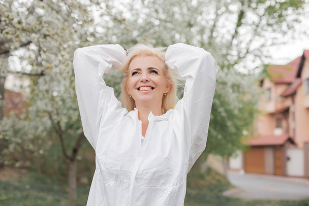 Ευτυχισμένη γυναίκα με λευκό προστατευτικό κοστούμι ανάμεσα στον κήπο της άνοιξης - Φωτογραφία, εικόνα