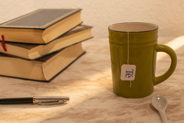 Taza de te con algunos libros al lado y una fuente pluma en un atardecer. - Foto, Imagen