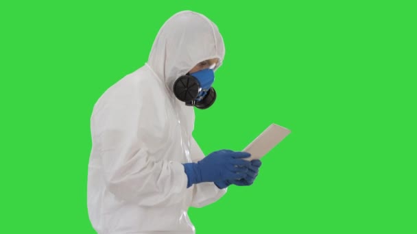 Tudós vagy docrot visel biológiailag veszélyes ruhák és védő maszkok segítségével digitális tabletta séta közben a zöld képernyőn, Chroma Key. - Felvétel, videó