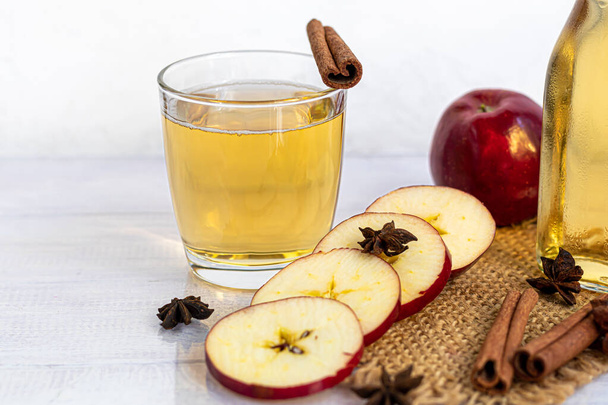 Healthy organic foods. Apple cider in a glass bowl and fresh red apples on a light background. In a glass of ice cubes and nearby cinnamon sticks. Copy space - Photo, Image