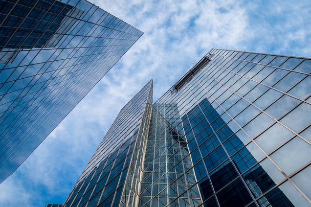 Высокие стеклянные небоскребы против голубого неба с белыми облаками, отражающимися в окнах зданий
. - Фото, изображение