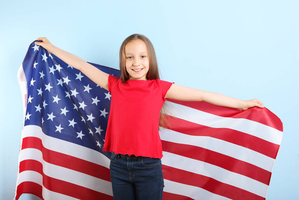 Πορτρέτο ενός μικρού θετικού κοριτσιού με μια αμερικανική σημαία στα χέρια της - Φωτογραφία, εικόνα