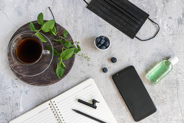 Quarantined work from home. Flatlay. Spring, green leaves, black coffee, notepad antiseptic blueberry and medical mask. - Fotoğraf, Görsel