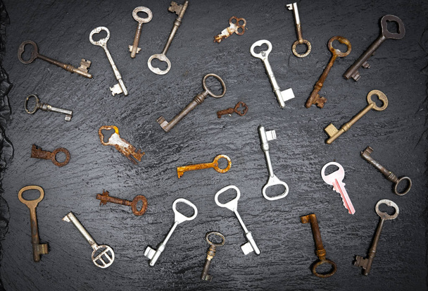 old keys of various shapes and shades seen from above creating a set of shapes on a black stone background - Photo, Image