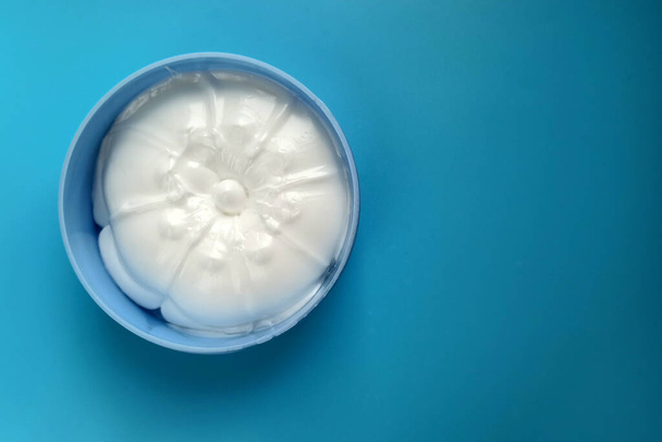 Body cream in a plastic container top view. White cream in a round box on a blue background. Cosmetics for the care of the skin of the hands, face and body. - Photo, Image