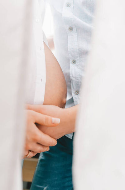 Closeup of couple's hand  on pregnant mother belly indoors. Vertical view - Photo, Image
