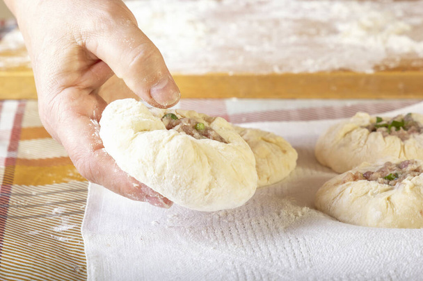 Las manos femeninas ponen las empanadas caseras de la masa cruda con el relleno de carne en la toalla de cocina. Primer plano
 - Foto, imagen