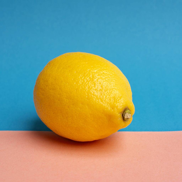A closeup of a lemon under the lights against a blue and peach background - Фото, изображение