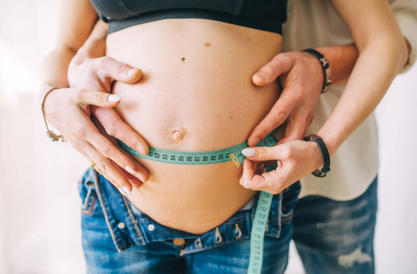 Lovely pregnant couple measuring belly. Cropped image of beautiful pregnant young woman touching her bare tummy while a man is measuring it. - Valokuva, kuva