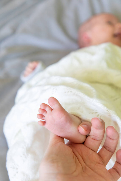 母親の手でベッドの上に寝そべっている赤ん坊のクローズアップ新生児の足 - 写真・画像