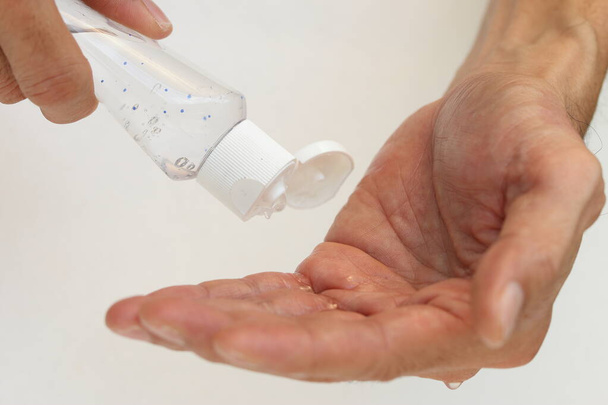 Руки з пляшкою з гелем для алкоголю, в той час як люди падають до рук, щоб застосувати захист від зародків та бруду на фоні білого кольору в концепції охорони здоров'я
. - Фото, зображення