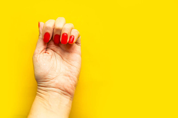 Chica mira sus uñas de esmalte rojo, vista superior, sin rostro, fondo amarillo brillante, espacio de copia
 - Foto, imagen