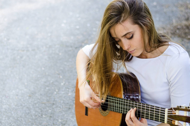 Young girl with long hair playing acoustic guitar outdoors. Copy space. - Photo, image