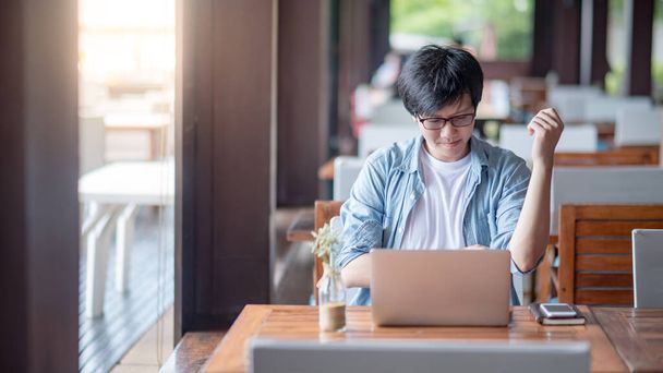 Young Asian freelance man using laptop computer in restaurant. Businessman in casual clothing doing online conference or telecommuting. Remote work from anywhere. Smart working with technology concept - Photo, Image