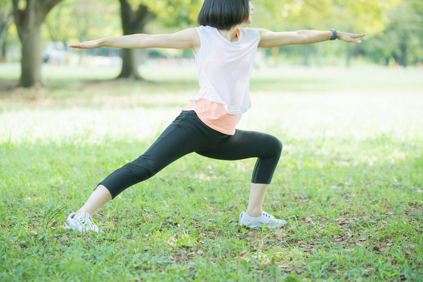 Азійська (японська) молода жінка, що тягнеться в парку, наповненому зеленню. - Фото, зображення