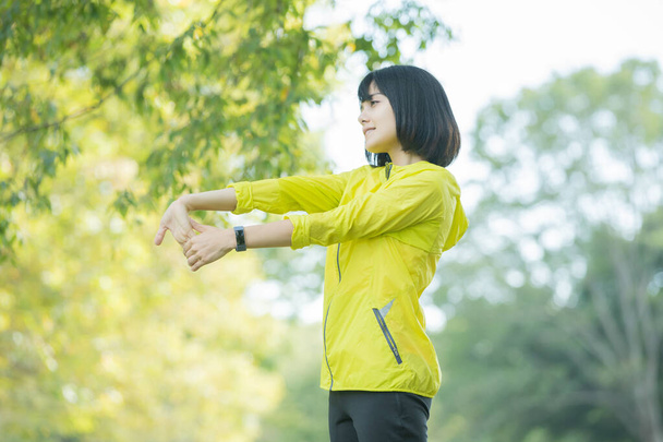 Ázsiai (japán) fiatal nő nyújtózkodik a parkban tele zöld - Fotó, kép