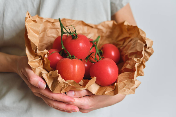 The girl holds tomatoes in her hands. Ripe fresh red tomatoes in paper packaging. Healthy food, organic vegetables. Natural vitamins, raw ingredient for eating. Handpicked bio tomato - Foto, immagini