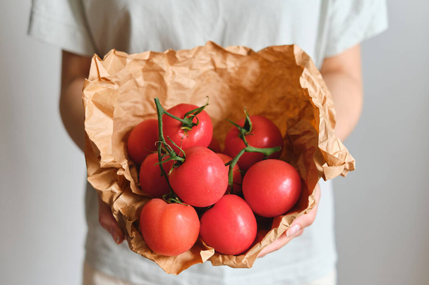 The girl holds tomatoes in her hands. Ripe fresh red tomatoes in paper packaging. Healthy food, organic vegetables. Natural vitamins, raw ingredient for eating. Handpicked bio tomato - Photo, image