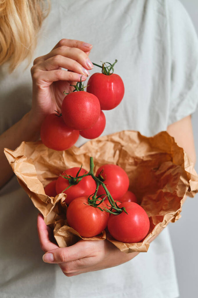The girl holds tomatoes in her hands. Ripe fresh red tomatoes in paper packaging. Healthy food, organic vegetables. Natural vitamins, raw ingredient for eating. Handpicked bio tomato - Zdjęcie, obraz