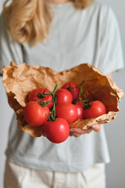 The girl holds tomatoes in her hands. Ripe fresh red tomatoes in paper packaging. Healthy food, organic vegetables. Natural vitamins, raw ingredient for eating. Handpicked bio tomato - Фото, зображення