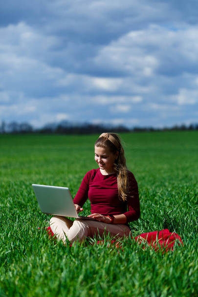 Kucağında dizüstü bilgisayarla çimenlerin üzerinde neşeli genç bir kız. O, ellerini kaldırdı ve güldü. Klasik bir öğrencinin yaşam tarzında mutluluk. Doğa üzerinde çalış. İyi bir iş gününden sonra dinlen.. - Fotoğraf, Görsel
