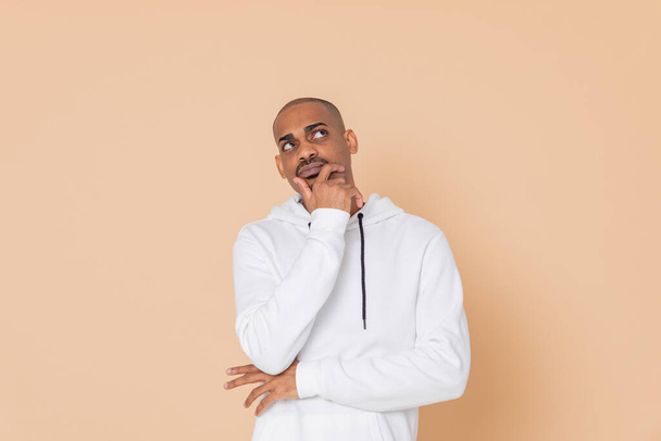 Pensive African guy with a white sweatshirt on a yellow background - Photo, Image