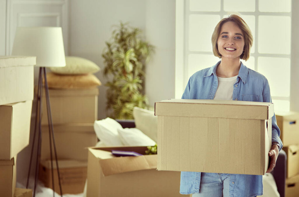 Portrait of pretty woman holding a box at new home - 写真・画像