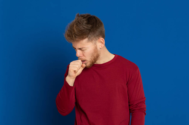 Attractive young guy with a red T-shirt on a blue background - Photo, Image