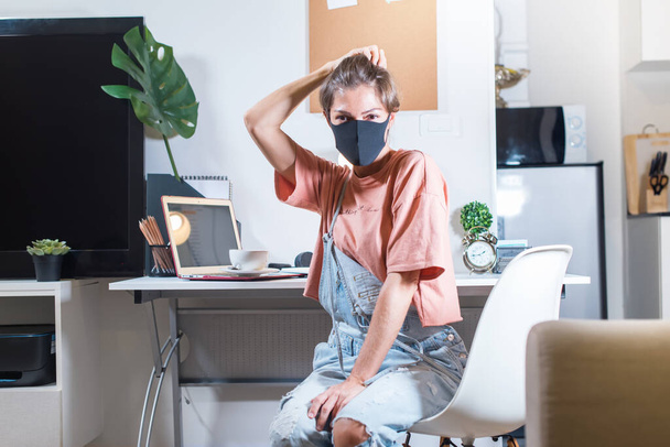 Woman is sitting in black protecting mask near table at home office. Working online during the quarantine. Self isolation. Networking. Crisis. Fighting against coronavirus. Stay at home - Fotoğraf, Görsel