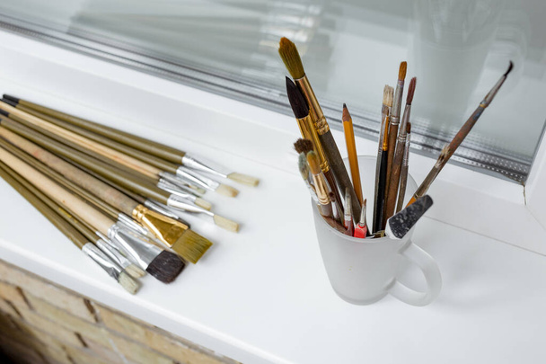 Escovas para pintura no peitoril da janela branca e escovas em um copo de vidro. Um processo de pintura. Hobby...
.  - Foto, Imagem