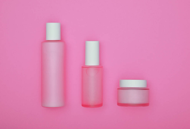 Close up conjunto de três cosméticos creme de cuidados da pele, loção e tônico garrafas sobre fundo rosa, vista superior elevada, diretamente acima
 - Foto, Imagem
