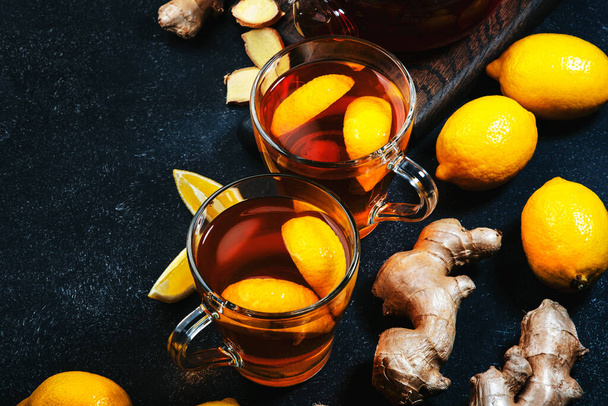 Healing black herbal tea with ginger, honey, lemon and sage. Immune booster drink in glass cup on black kitchen table background with copy space. Top view - Foto, Imagem