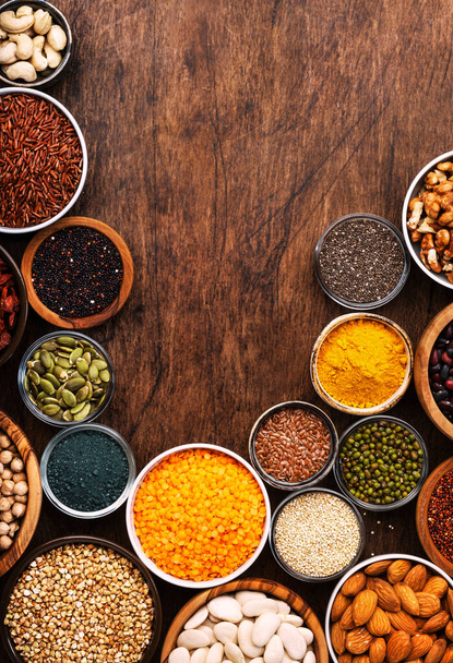 Superfoods, legumes, nuts, seeds and cereals set in bowls on wooden background. Superfood as chia, spirulina, beans, goji berries, quinoa, turmeric, mung bean, buckwheat, lentils, flax seed, wild rice and almond. Copy space, top view - Photo, Image
