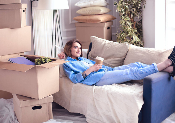 Young woman of moving boxes lying on sofa in new house - Foto, immagini