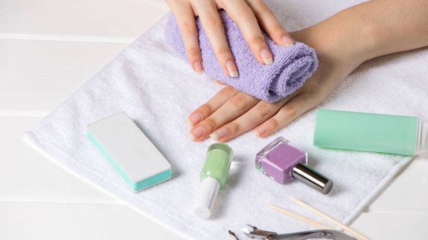 Manicure. The woman wipes her hand with a towel. Manicure tools, nail polishes. Home nail care, SPA, beauty. Long natural nails. Beauty salon. - Фото, изображение