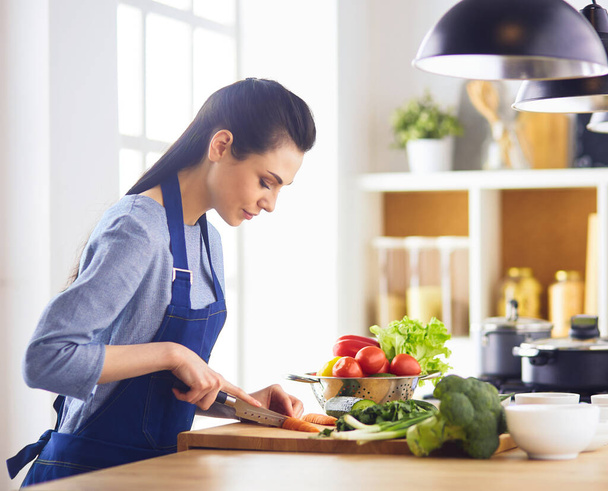 Young woman cutting vegetables in kitchen at home - Foto, Bild