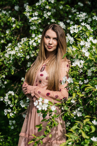 portrait of a beautiful girl in a pink dress on a background of white flowers in a blooming apple orchard - Zdjęcie, obraz