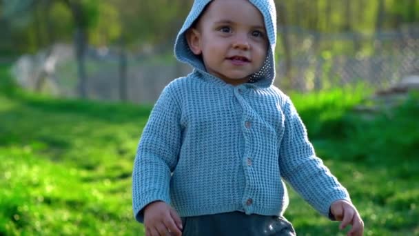 Cute portrait of walking smiling little baby boy waving hello in park or green garden. First steps. Lovely son, family, toddler concept. - Footage, Video