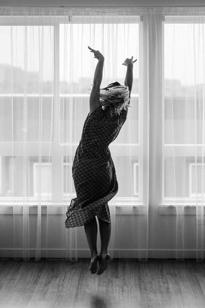 Concetto in bianco e nero, danze da donna in maxi abito davanti alla finestra. Ballerina sta ballando. Mosse da ballo. Self isolamento rimanere a casa coronavirus.Dancer mostra vicini di casa i suoi movimenti danzanti.
 - Foto, immagini