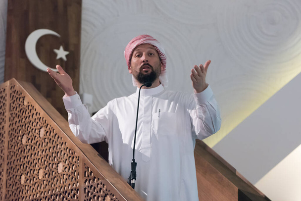 Muslimit nuori arabialainen imaami pitää puheen perjantai-iltapäivän rukouksesta moskeijassa. Muslimit ovat kokoontuneet perjantai-iltapäivän rukoukseen moskeijassa ja kuuntelevat imaamin puhetta. - Valokuva, kuva