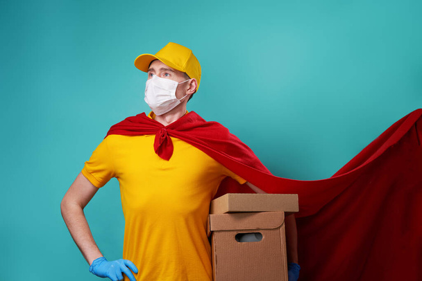 Courier with boxes is wearing urgical face mask in superhero cloak. - Fotó, kép