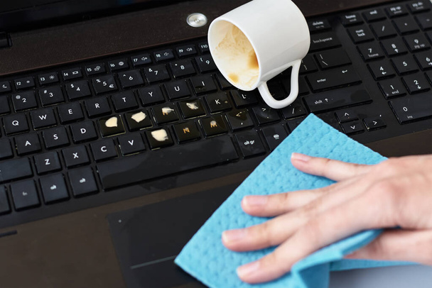 Ręcznie czyści rozlaną kawę na klawiaturze laptopa z szmatą - Zdjęcie, obraz