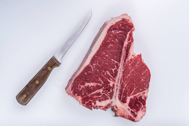 Ein T-Bone Steak, das gerade auf einem Metzgertisch neben einem Vintage-Knochenmesser geschnitten wurde - Foto, Bild