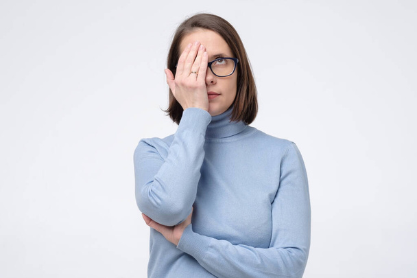 Mujer caucásica seria en gafas cubrió su cara media mano aislada en la pared blanca
. - Foto, Imagen