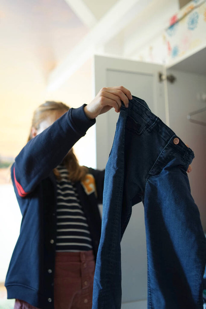 Mladá dívka si vybírá oblečení ze skříně. Dítě přemýšlí, co si vzít na sebe před šatníkem s mnoha možnostmi šatů na ramínka a zásuvky. - Fotografie, Obrázek