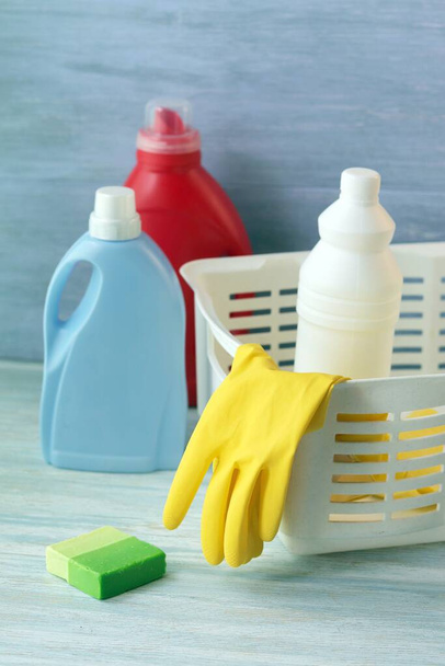  Vloeibare wasmiddelen in plastic flessen, rubberen handschoenen voor het reinigen van het huis op een houten tafel, levering aan huis - Foto, afbeelding